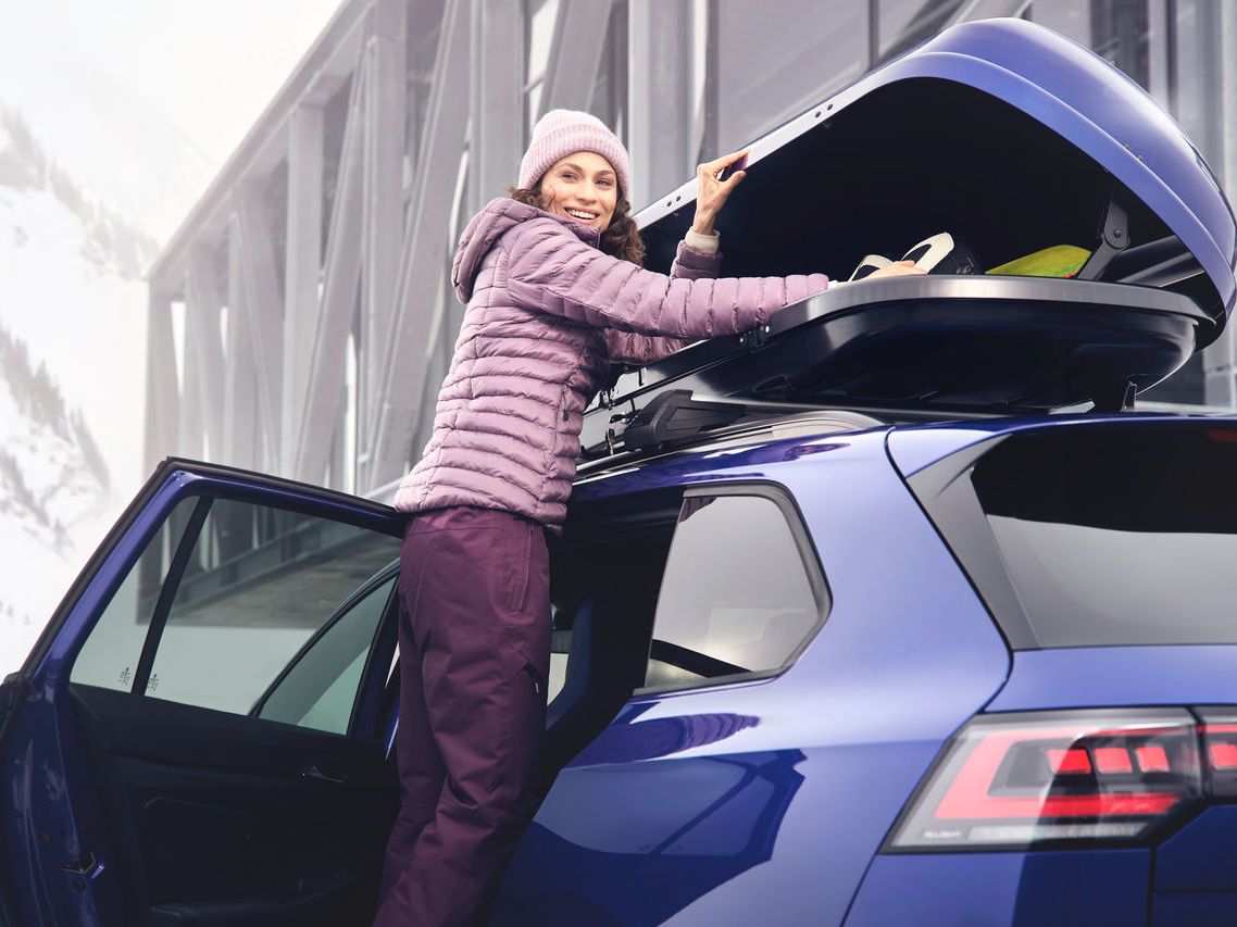 Eine Frau öffnet eine auf einem blauen Volkswagen befestigte Dachbox.