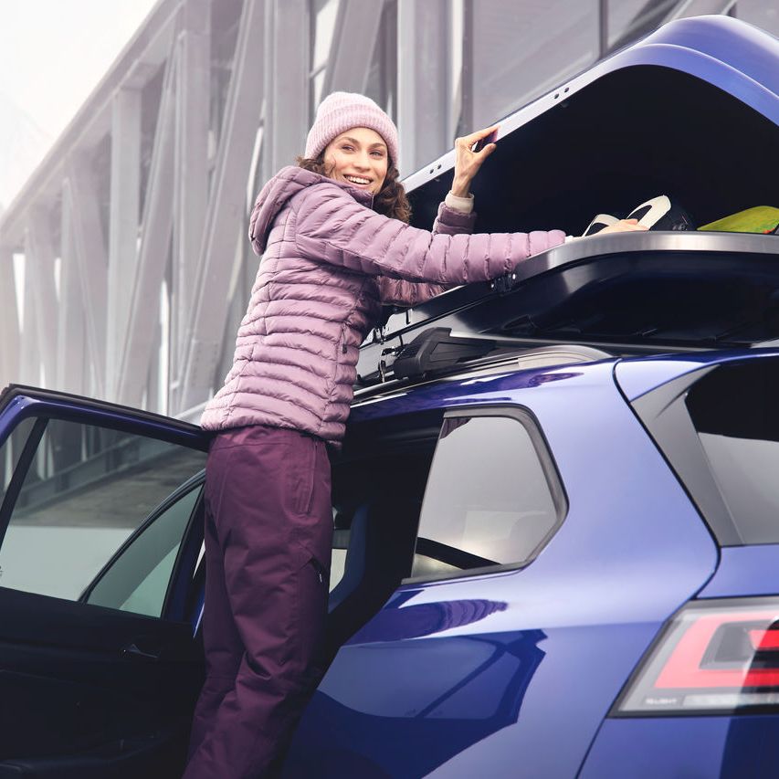 Eine Frau öffnet eine auf einem blauen Volkswagen befestigte Dachbox.
