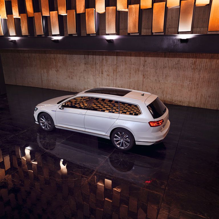 Ein weißer VW Passat steht in einer Halle mit dunklem Boden und wird von der Decke angestrahlt.