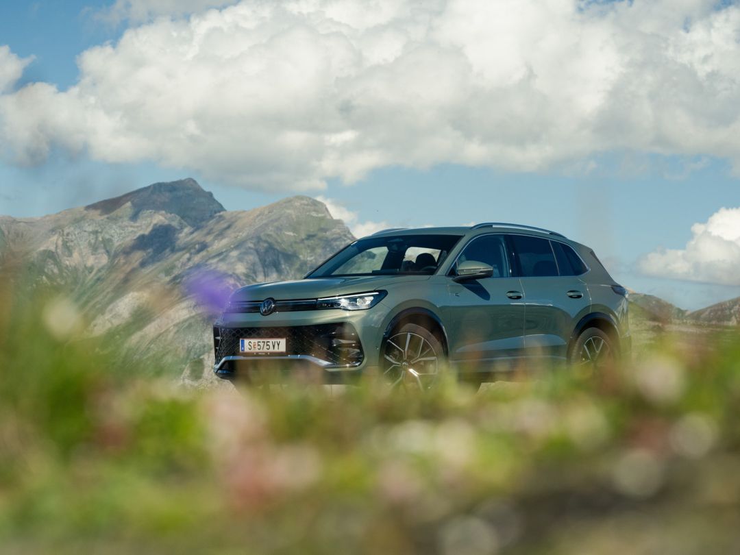 Ein olivgrüner VW Tiguan R-Line von vorne vor Bergpanorama