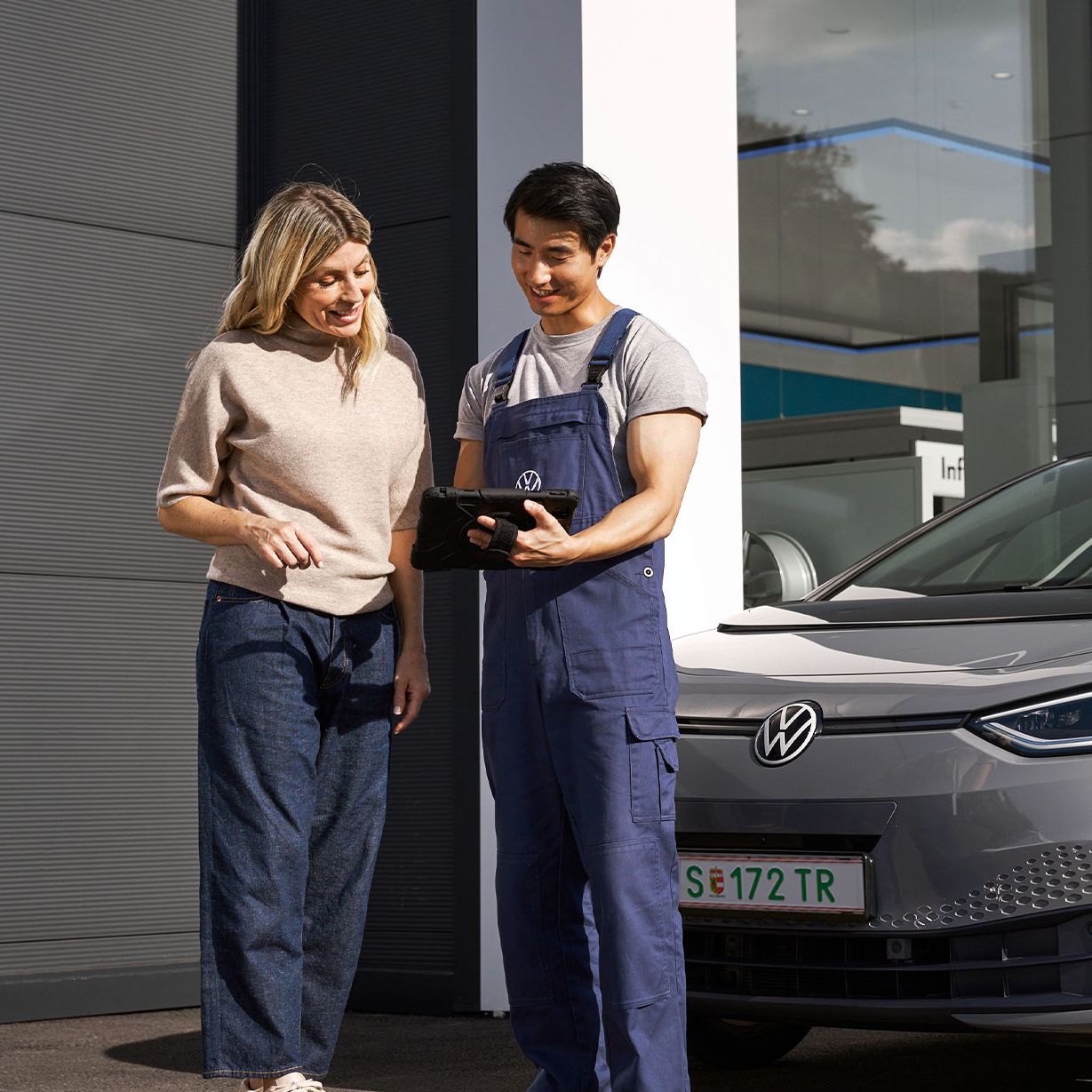 Ein Volkswagen Techniker und eine Kundin stehen vor einem grauen Volkswagen ID.3