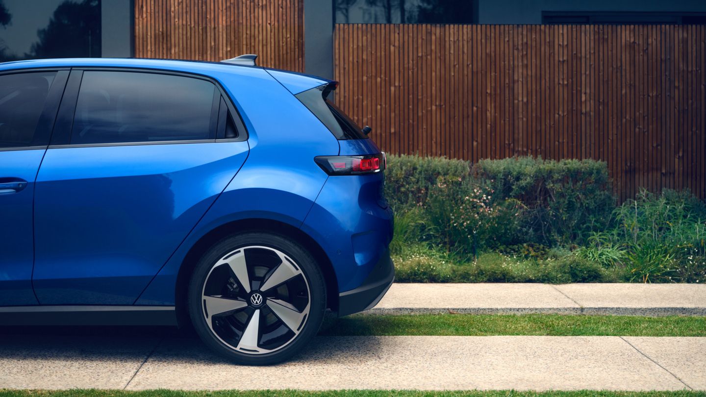 Seitliche Heckansicht eines blauen VW ID. Polo Style, der vor einem Wohnhaus mit begrünter Einfahrt steht.