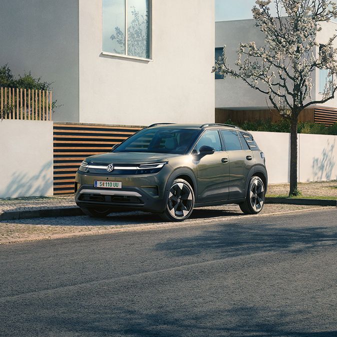 Ein grüner VW ID. Cross parkt in einer Parkbucht eines Wohngebiets mit blühenden Bäumen.