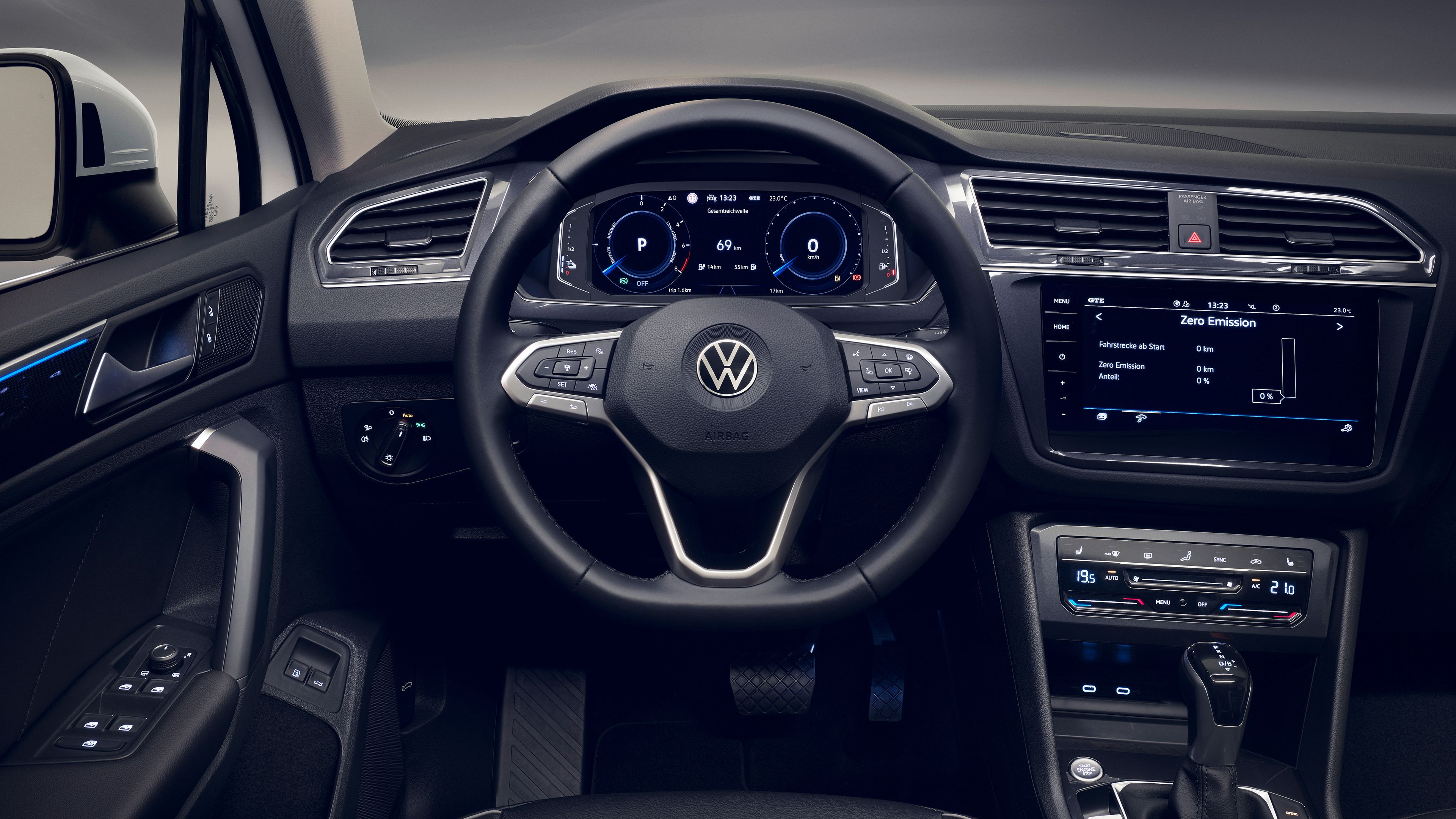 Das Bild zeigt das Cockpit eines Tiguan Vorgängermodells, einschließlich Lenkrad mit Volkswagen-Logo, digitale Tachometer und Navigations-Display. Unterhalb des Bildschirms befindet sich die Klimaanlagensteuerung sowie ein Handschaltgetriebe. Die Instrumententafel ist schwarz und das Design wirkt elegant.