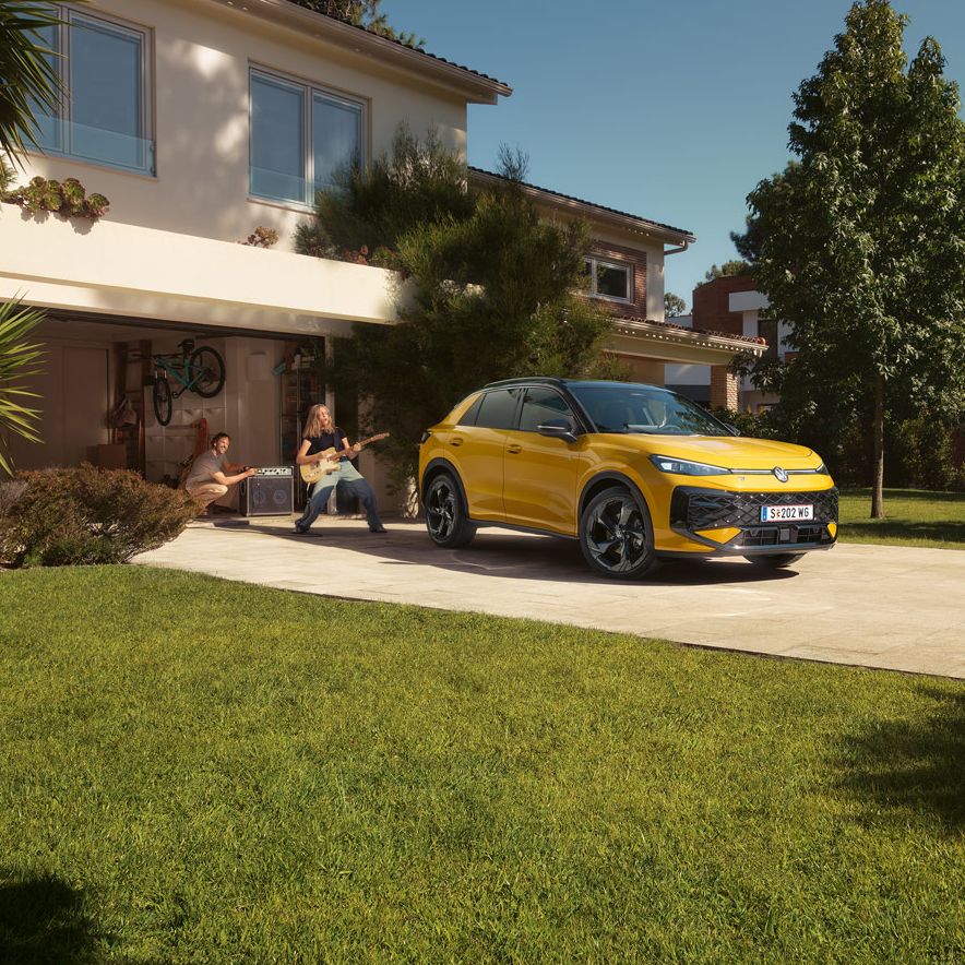 Ein gelber VW T-Roc R-Line steht vor der Garage, ein Mädchen spielt Gitarre, ihr Vater steuert den Lautsprecher.