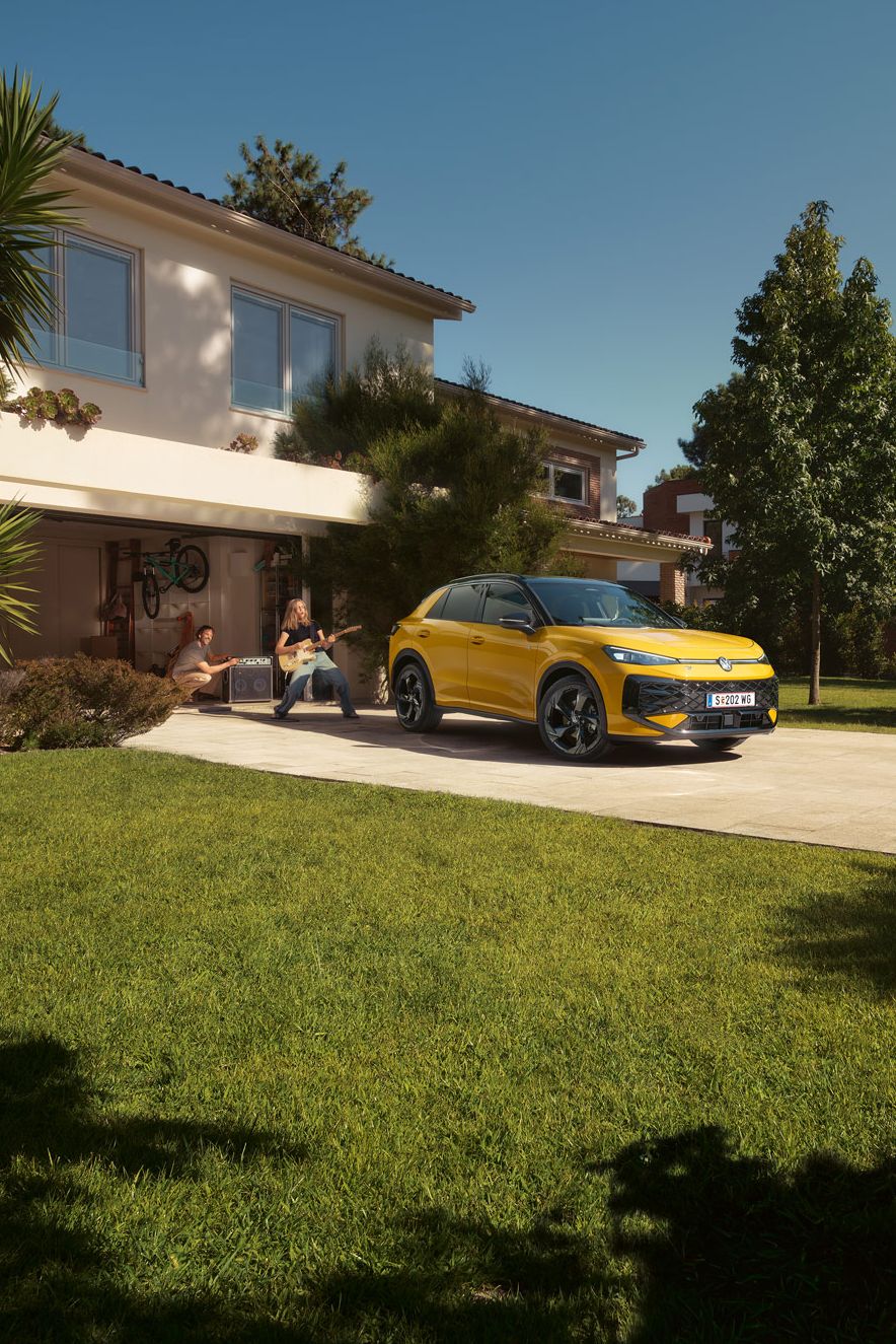 Ein gelber VW T-Roc R-Line steht vor der Garage, ein Mädchen spielt Gitarre, ihr Vater steuert den Lautsprecher.