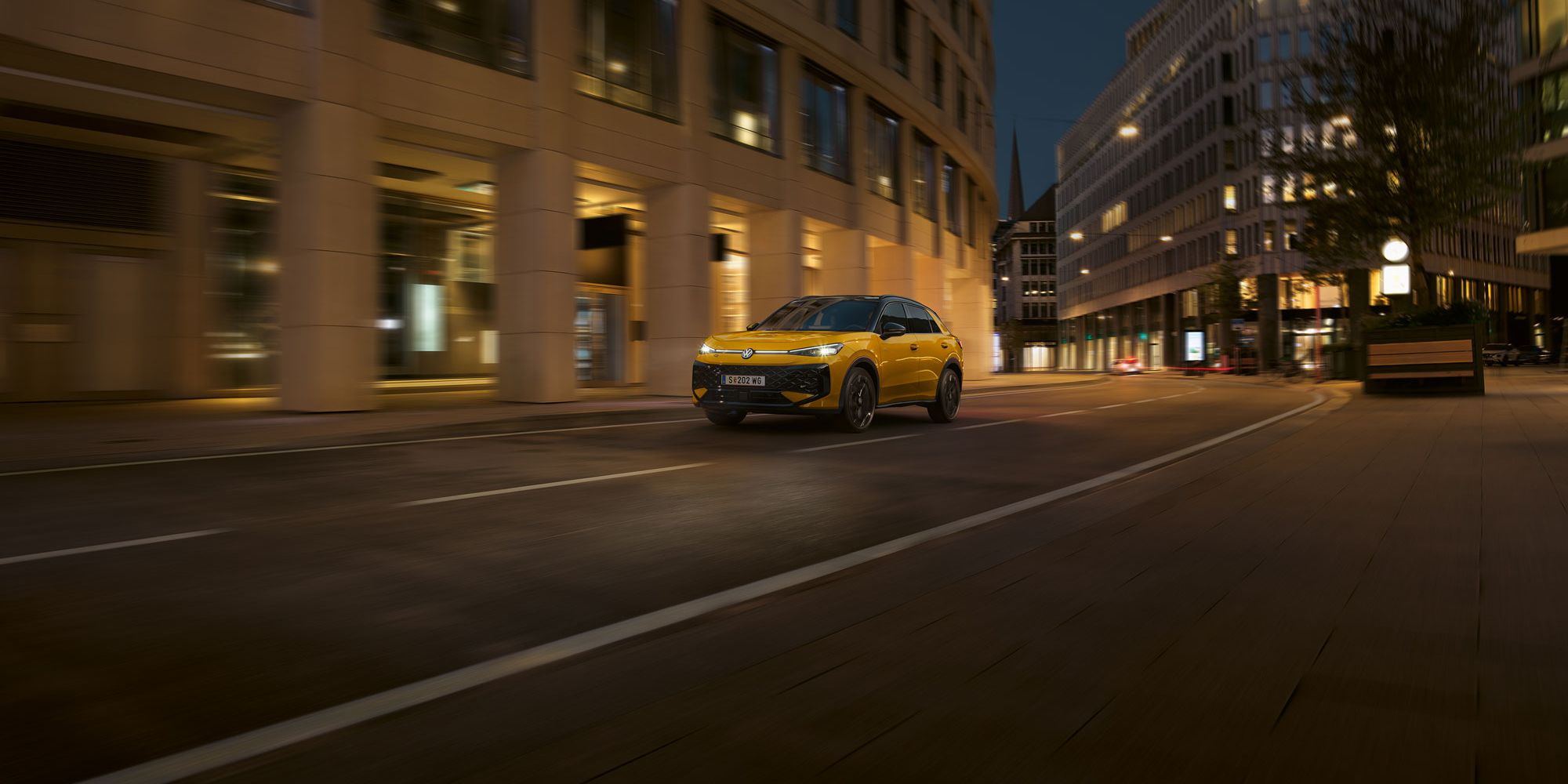 Ein gelber VW T-Roc R-Line fährt nachts durch eine urbane Umgebung.