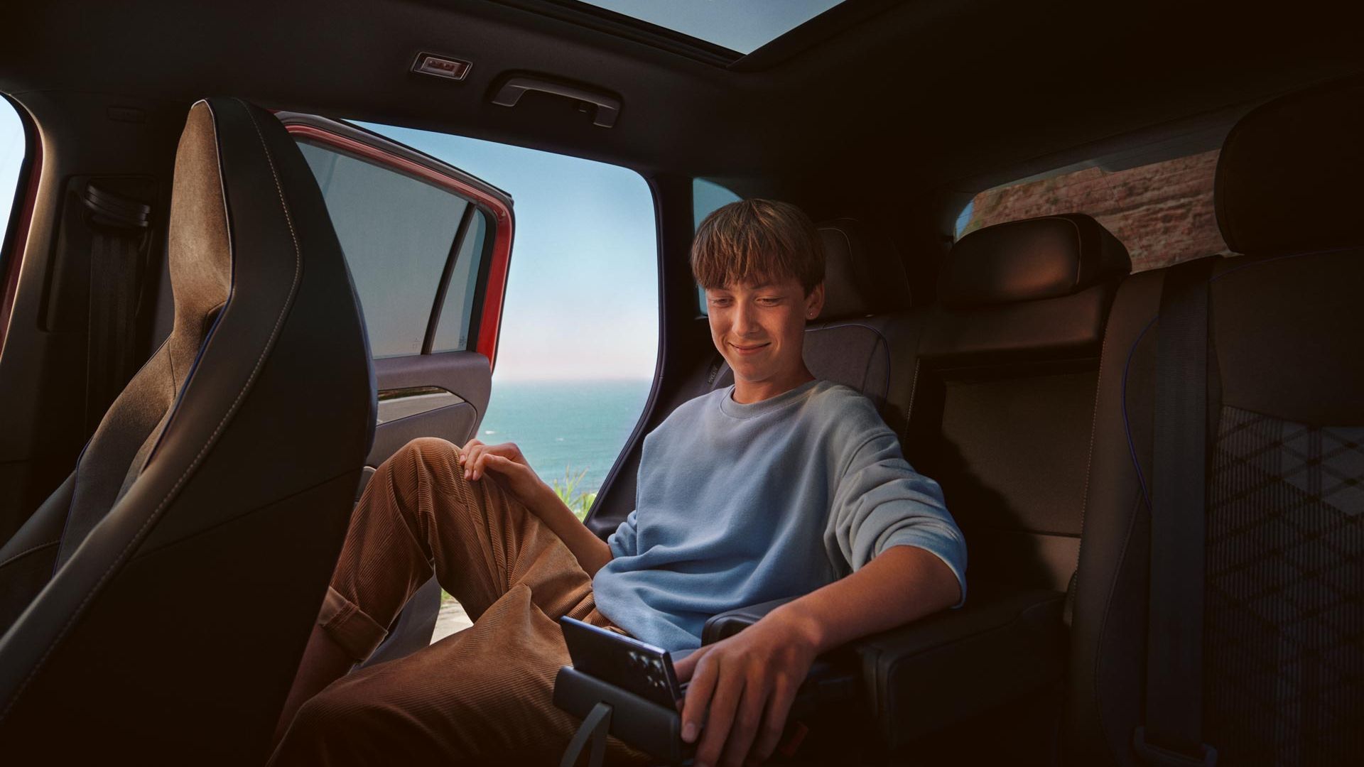 Jugendlicher sitzt auf Rückbank im VW Tiguan und bedient Smartphone in Halterung