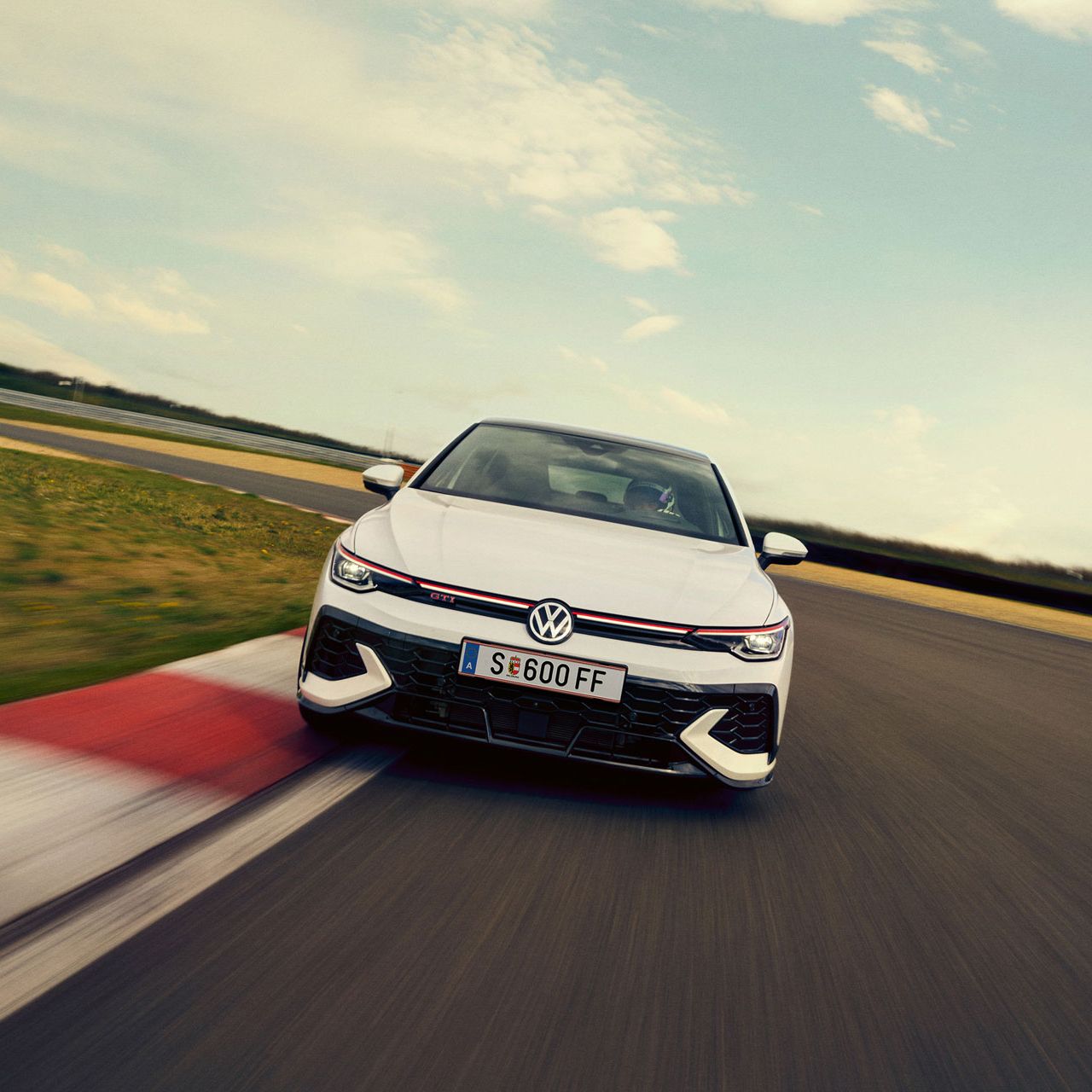 Frontansicht eines weißen VW Golf GTI Clubsport, der auf einer Rennstrecke in eine Kurve fährt.