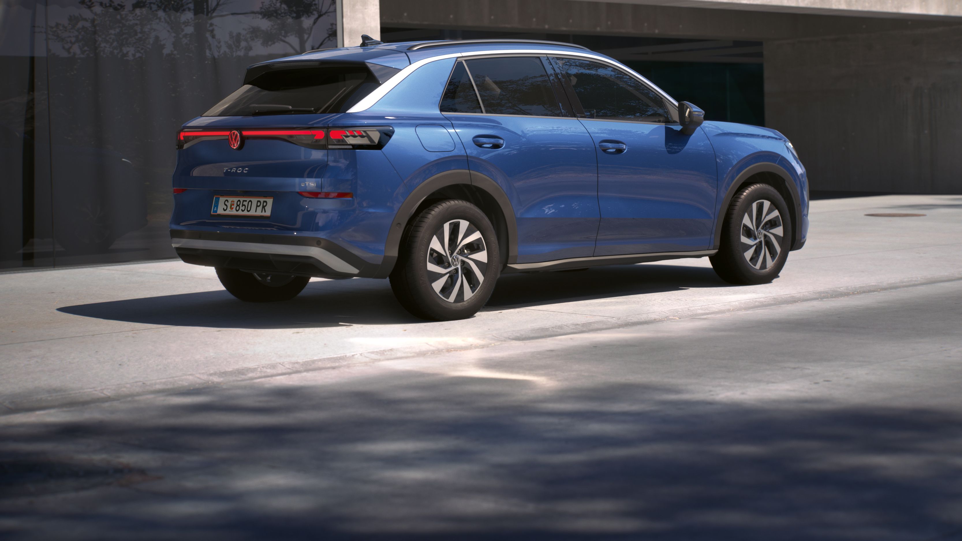 Eine 3/4-Rückansicht eines blauen Volkswagen T-Roc Life, parkend vor einem Gebäude.