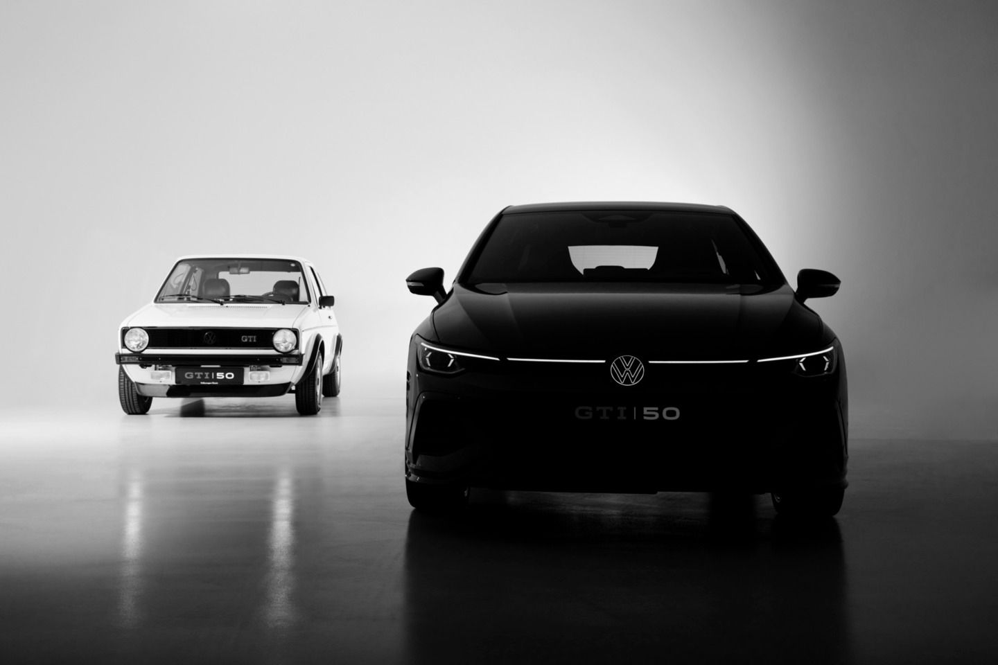 Ein Golf GTI Editon 50 und ein Golf 1 GTI stehen nebeneinander. Blick auf die Frontpartie beider Autos.