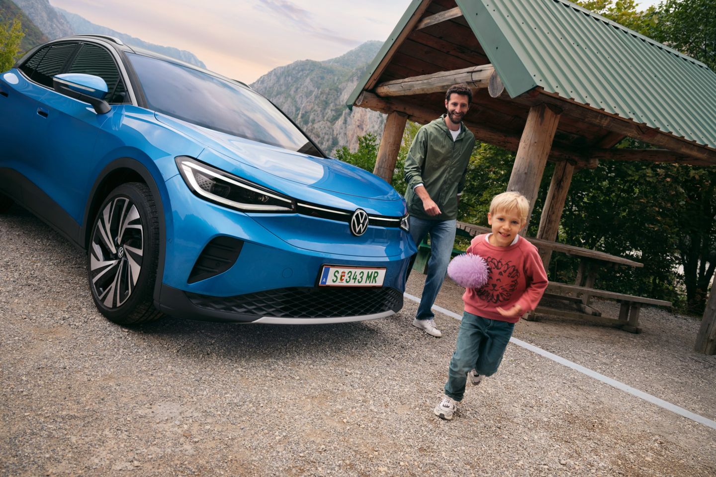 Vater und Sohn spielen mit einem Ball, daneben steht ein blauer VW ID.4.
