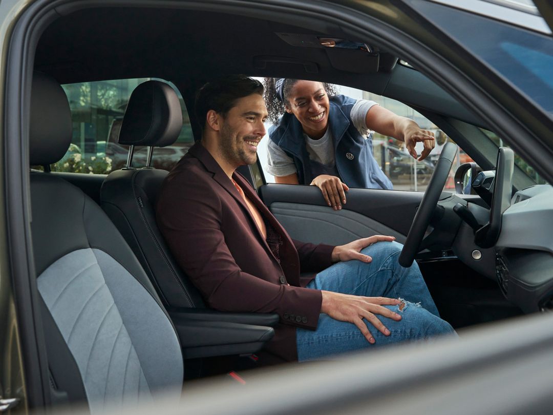 Eine Servicemitarbeiterin zeigt einem Mann im VW ID.5 eine Funktion im Infotainmentsystem.