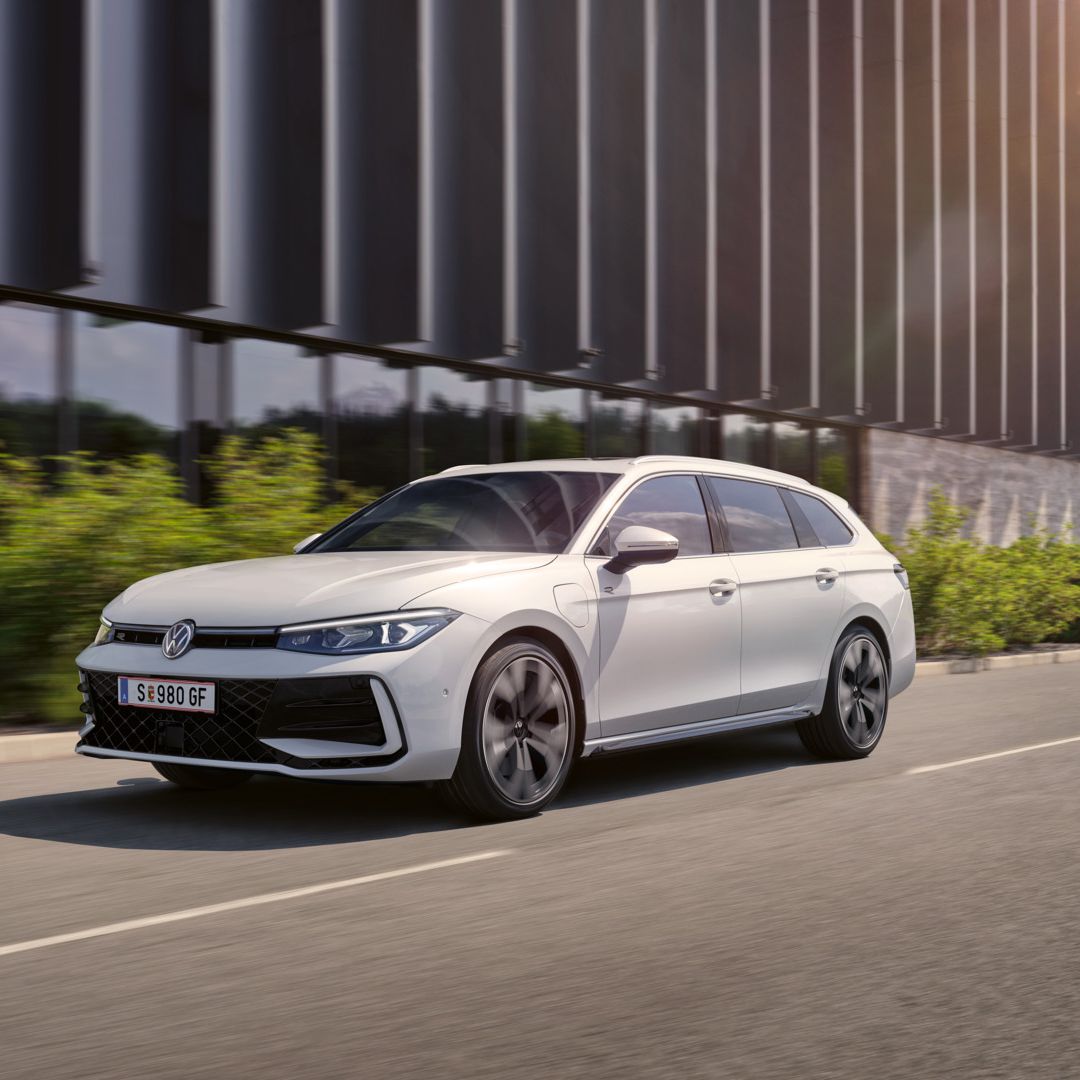 Ein weißer VW Passat fährt vor einem modernen Bürogebäude entlang.
