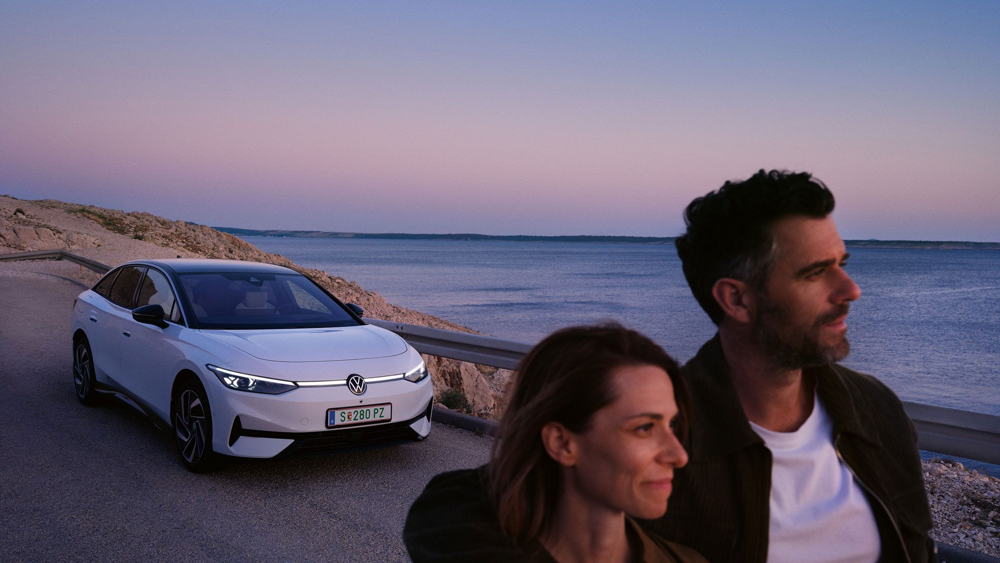 Ein Pärchen läuft am Meer entlang, im Hintergrund parkt ein ID.7 