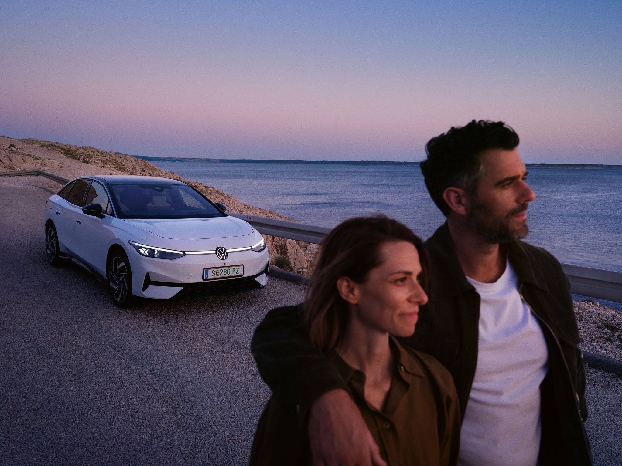 Ein Pärchen läuft am Meer entlang, im Hintergrund parkt ein ID.7 