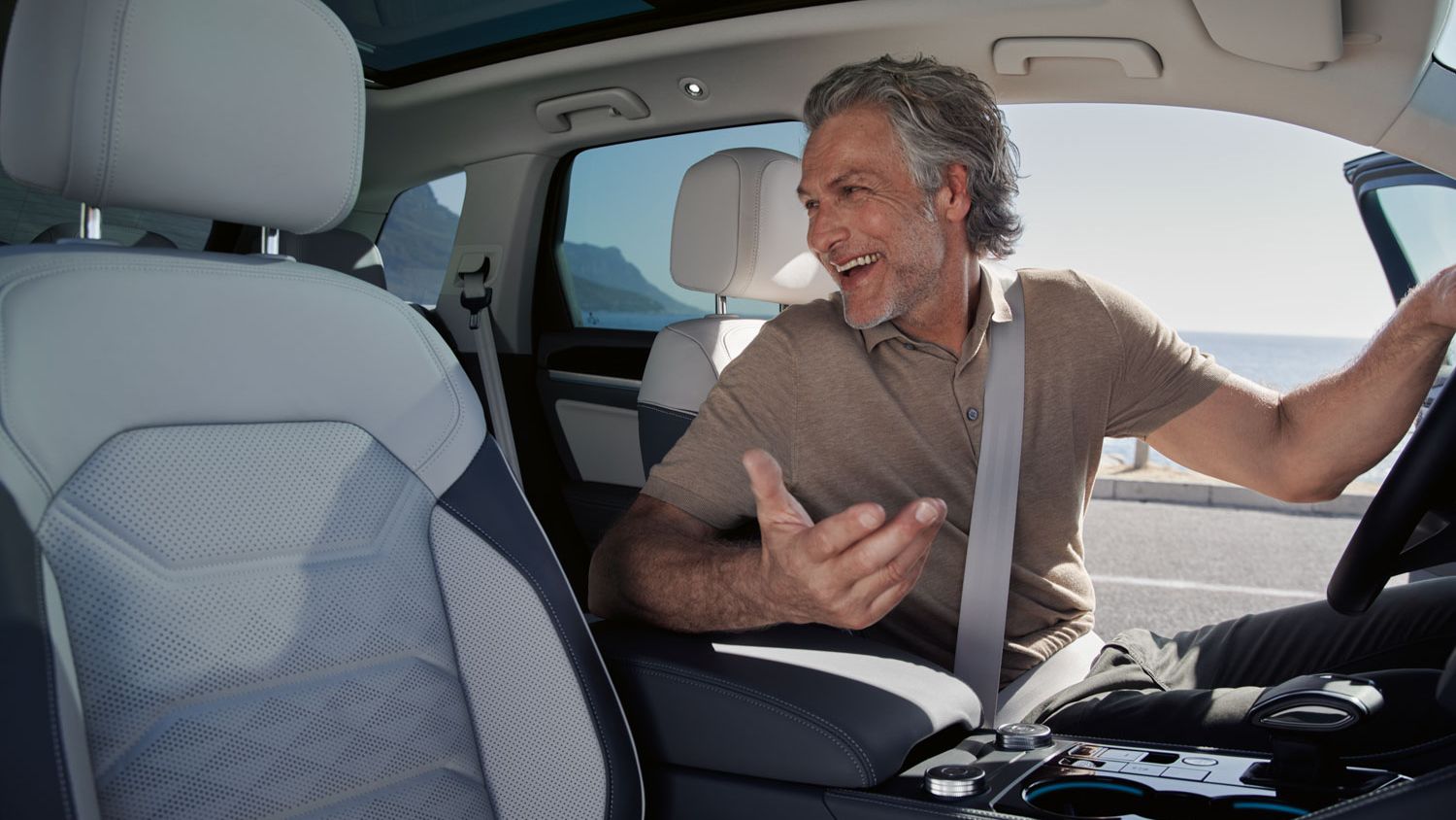 Ein Mann auf dem Vordersitz eines parkenden VW Touareg Elegance unterhält sich mit einer Person auf dem Rücksitz. 