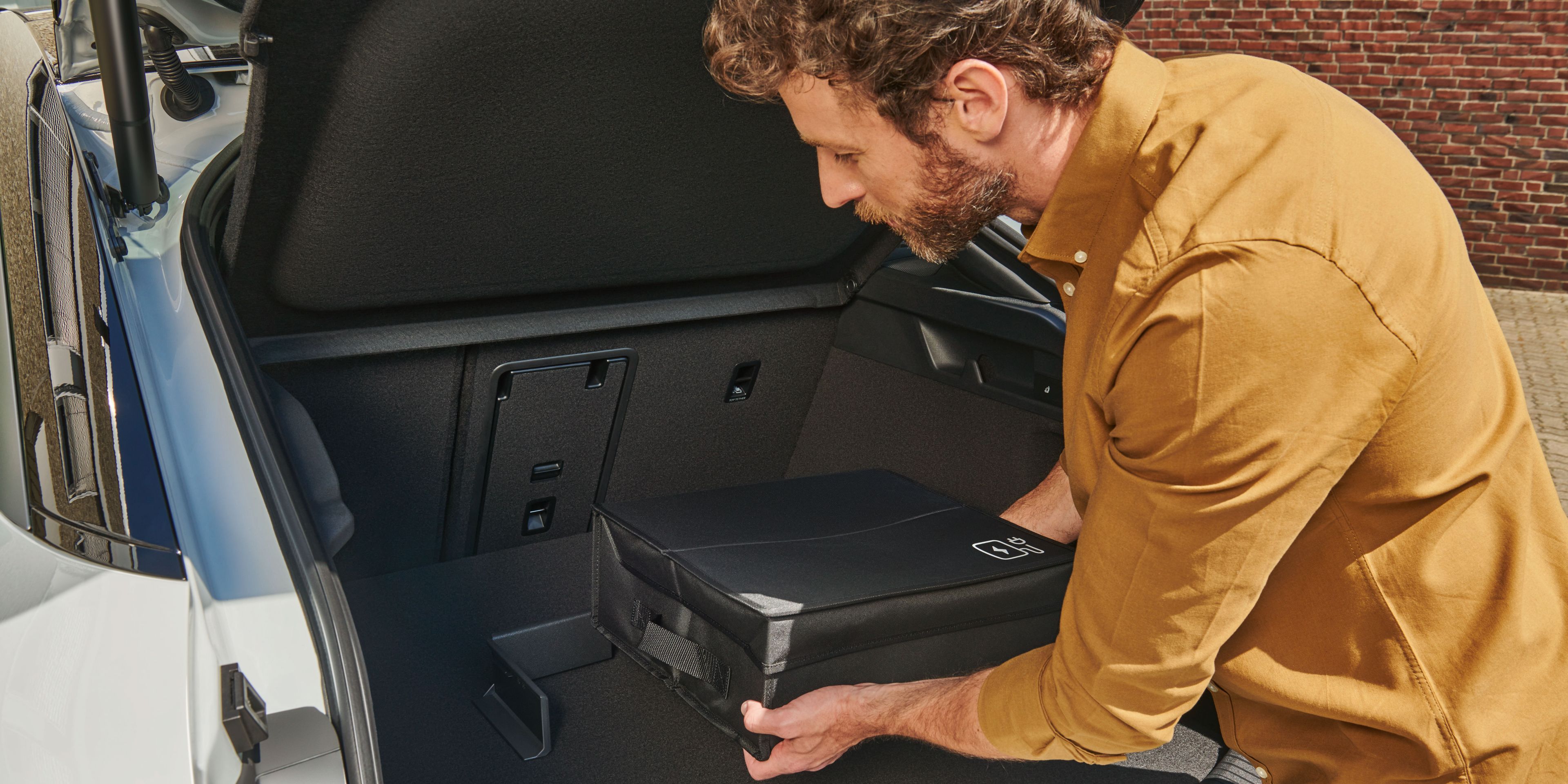 Ein Mann befestigt eine Tasche mit Volkswagen Original Cargo Elementen im Kofferraum eines Volkswagen ID.7.