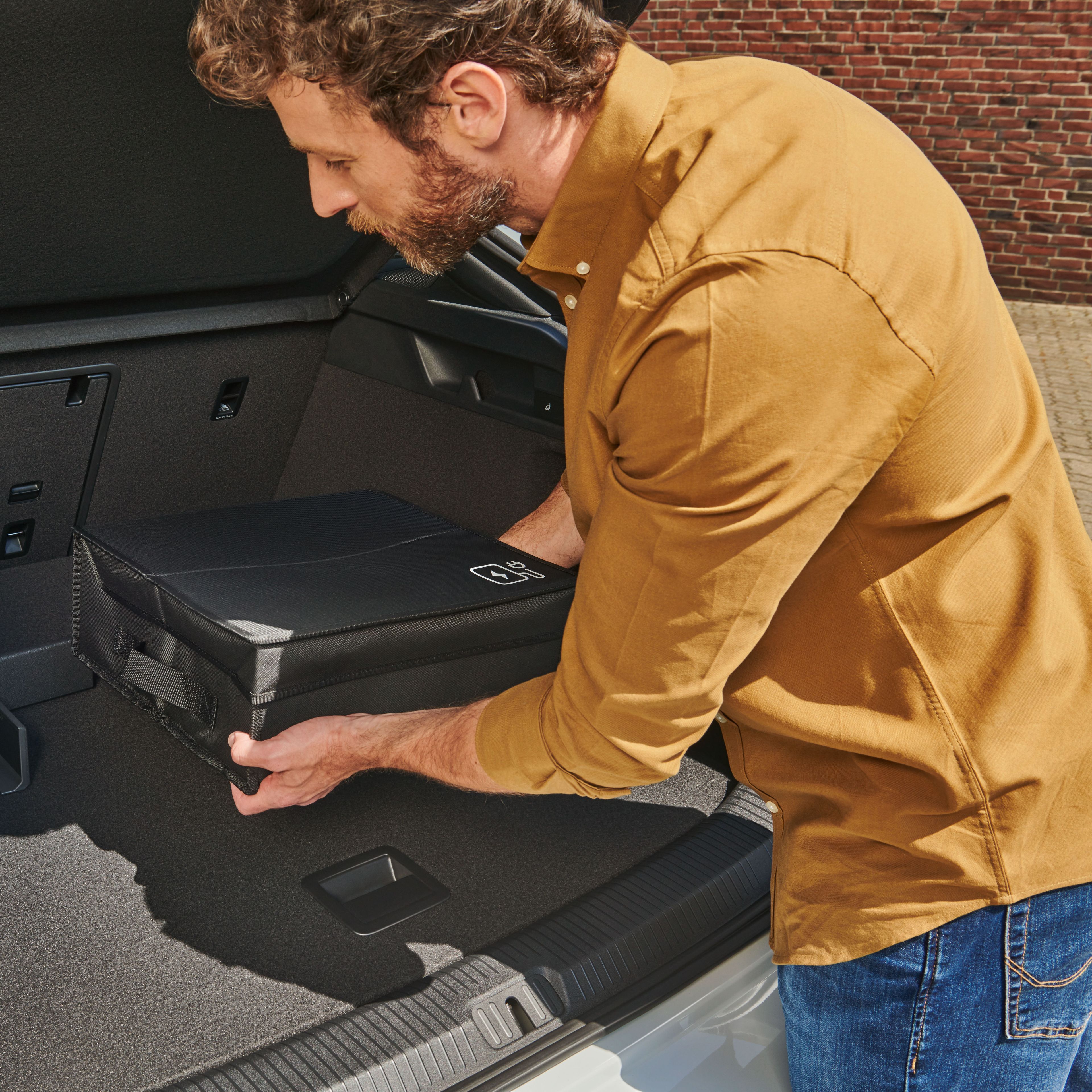 Ein Mann befestigt eine Tasche mit Volkswagen Original Cargo Elementen im Kofferraum eines Volkswagen ID.7.