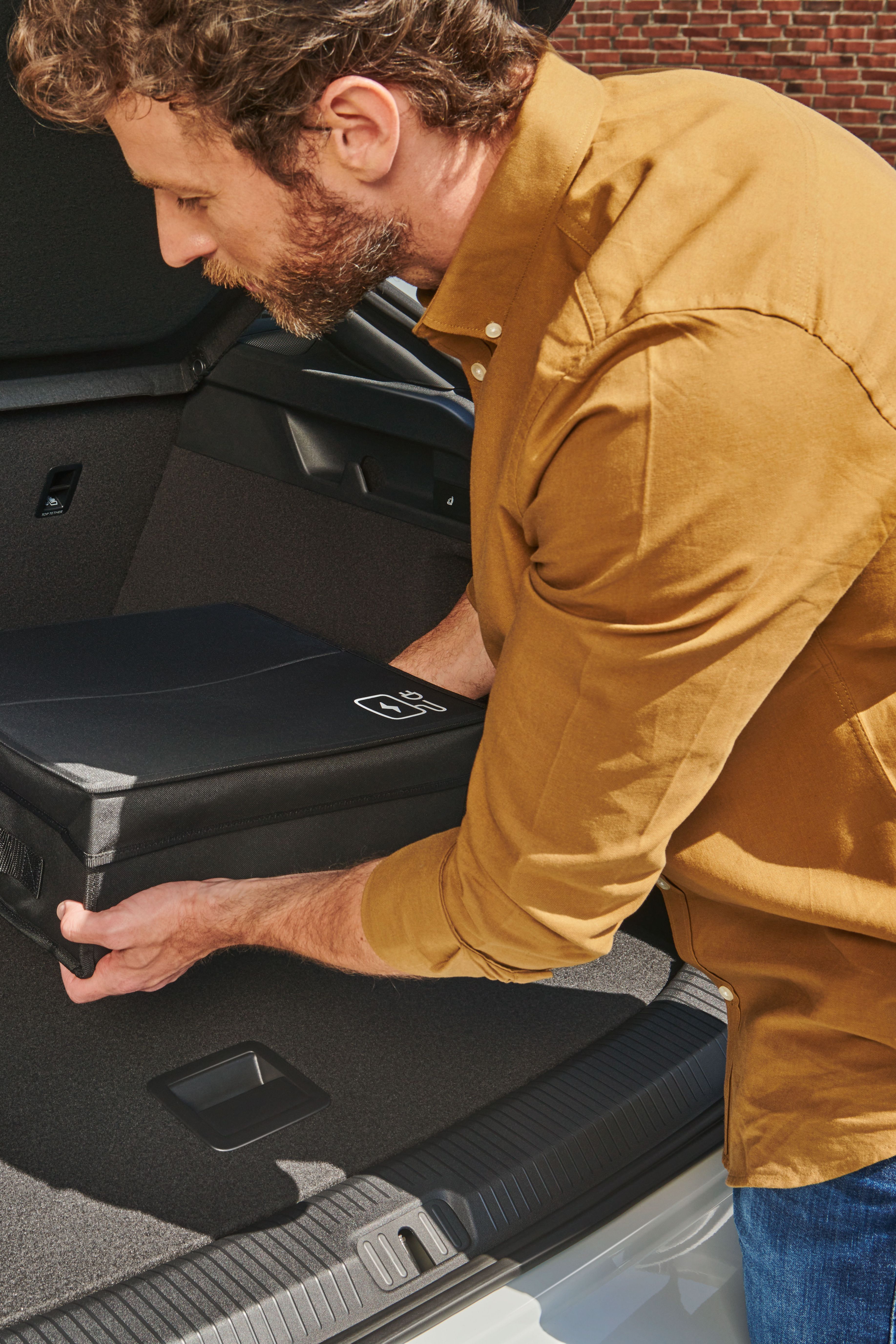 Ein Mann befestigt eine Tasche mit Volkswagen Original Cargo Elementen im Kofferraum eines Volkswagen ID.7.