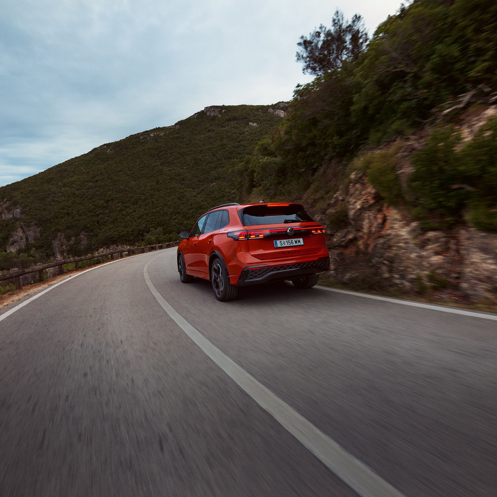 Roter VW Tiguan in Heckansicht fährt durch eine bergige Landschaft.