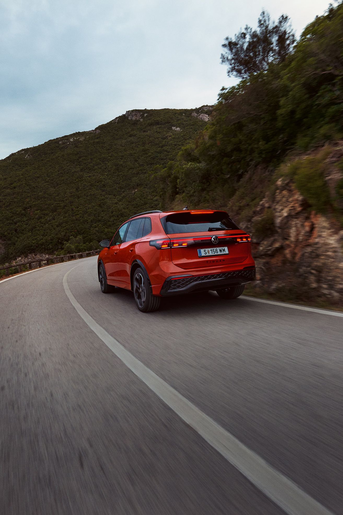 Roter VW Tiguan in Heckansicht fährt durch eine bergige Landschaft.