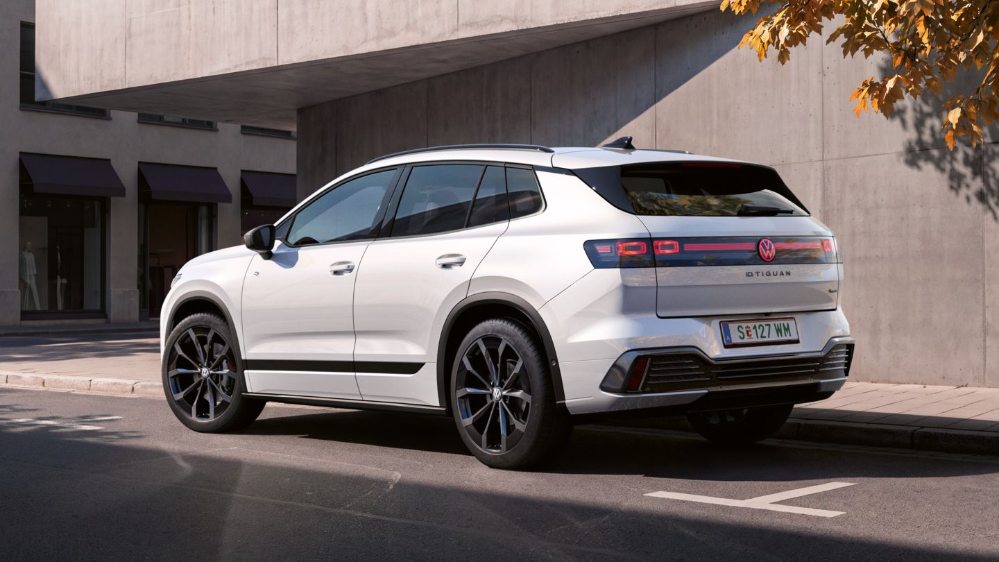 Seitliche Heckansicht eines weißen VW ID. Tiguan R-Line geparkt vor einem modernen Gebäude.