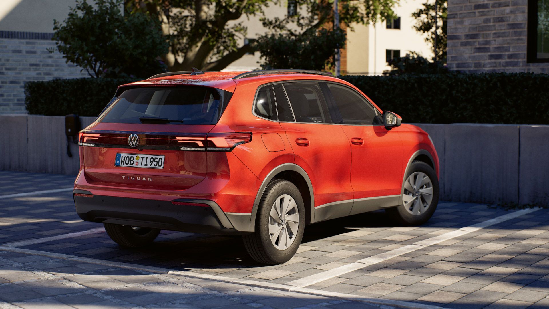 Roter Volkswagen Tiguan steht rückwärts in einer Parklücke auf einem gepflasterten Parkplatz. Im Hintergrund sind ein modernes Gebäude, eine Mauer und Bäume zu sehen, die eine ruhige Wohn- oder Stadtumgebung andeuten.