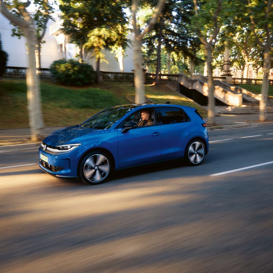 Ein blauer VW ID. Polo fährt auf einer Straße, im Hintergrund eine Reihe Bäume und Häuser.