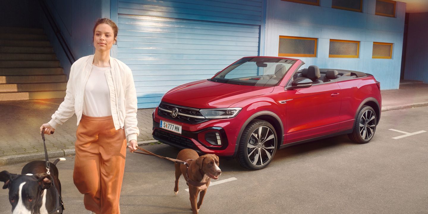Frau geht mit zwei Hunden and der Leinen von einem roten VW T-Roc Cabrio weg