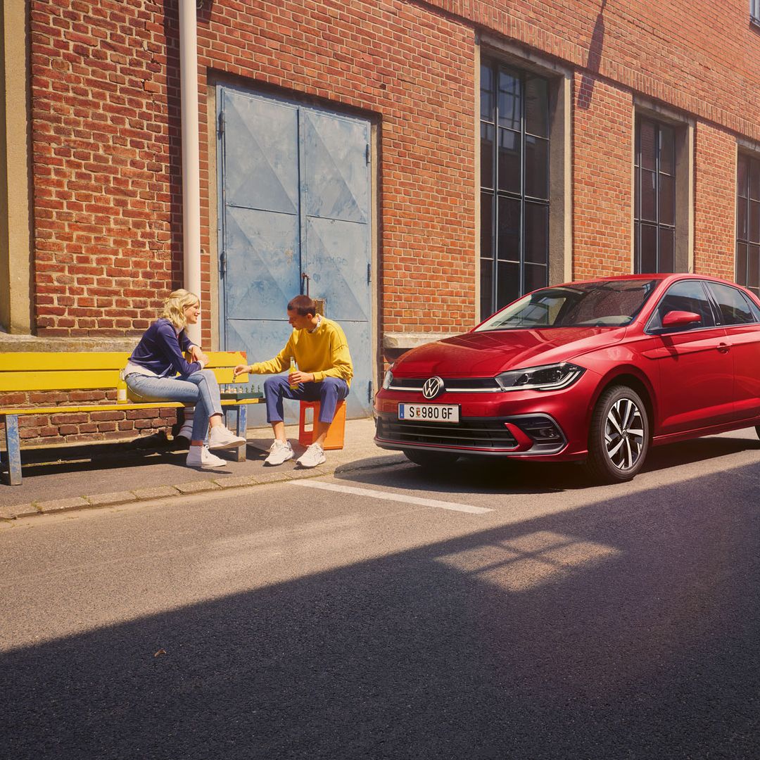 Zwei Personen spielen Schach vor einem roten VW Polo Style, der vor einem Fabrikgebäude parkt.