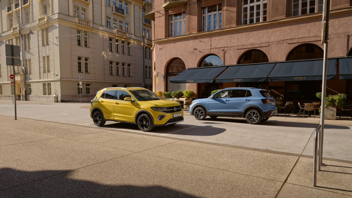Ein gelber und ein blauer VW T-Cross fahren auf einer Straße aneinander vorbei.