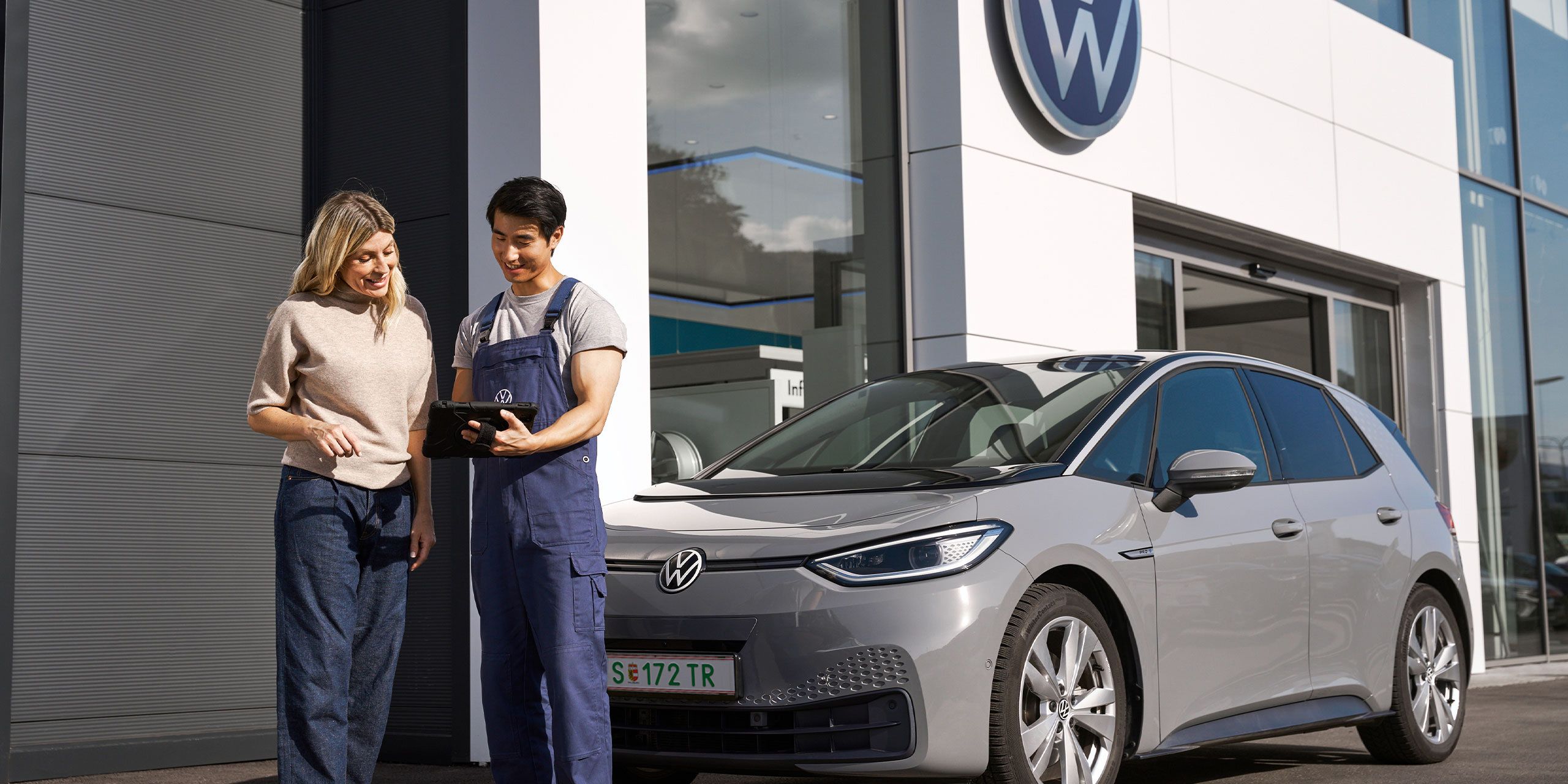 Ein Volkswagen Techniker und eine Kundin stehen vor einem grauen Volkswagen ID.3