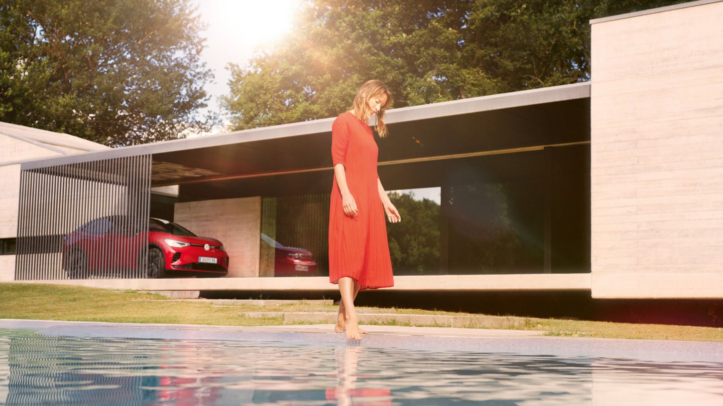 Ein roter ID.5 GTX steht vor einem modernen Privathaus, im Vordergrund hält eine Frau ihre Füße in den Pool. 