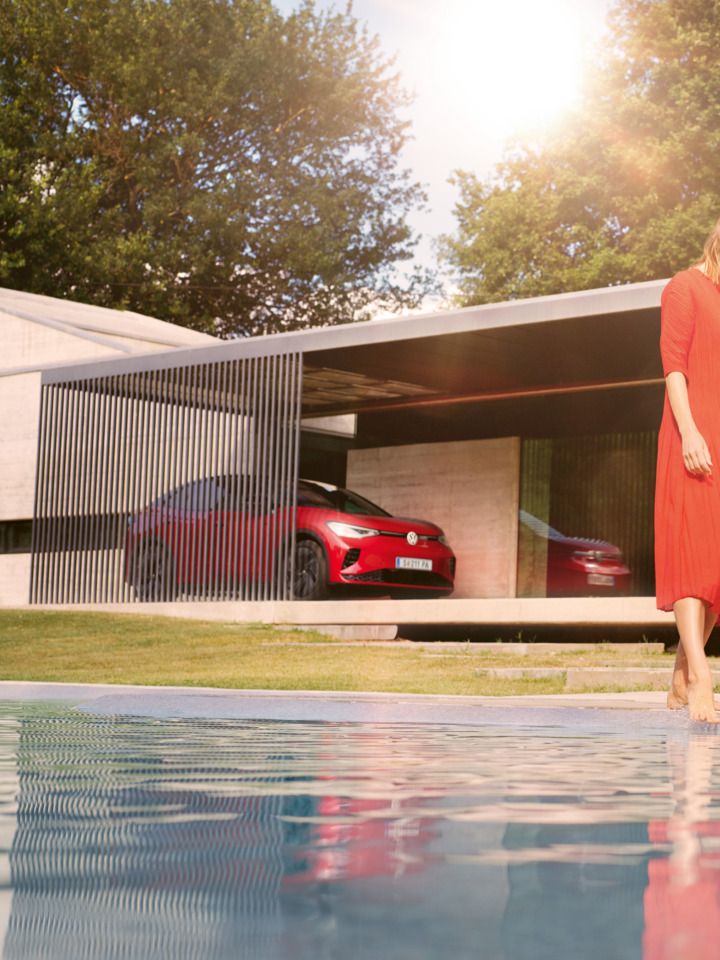 Ein roter ID.5 GTX steht vor einem modernen Privathaus, im Vordergrund hält eine Frau ihre Füße in den Pool. 