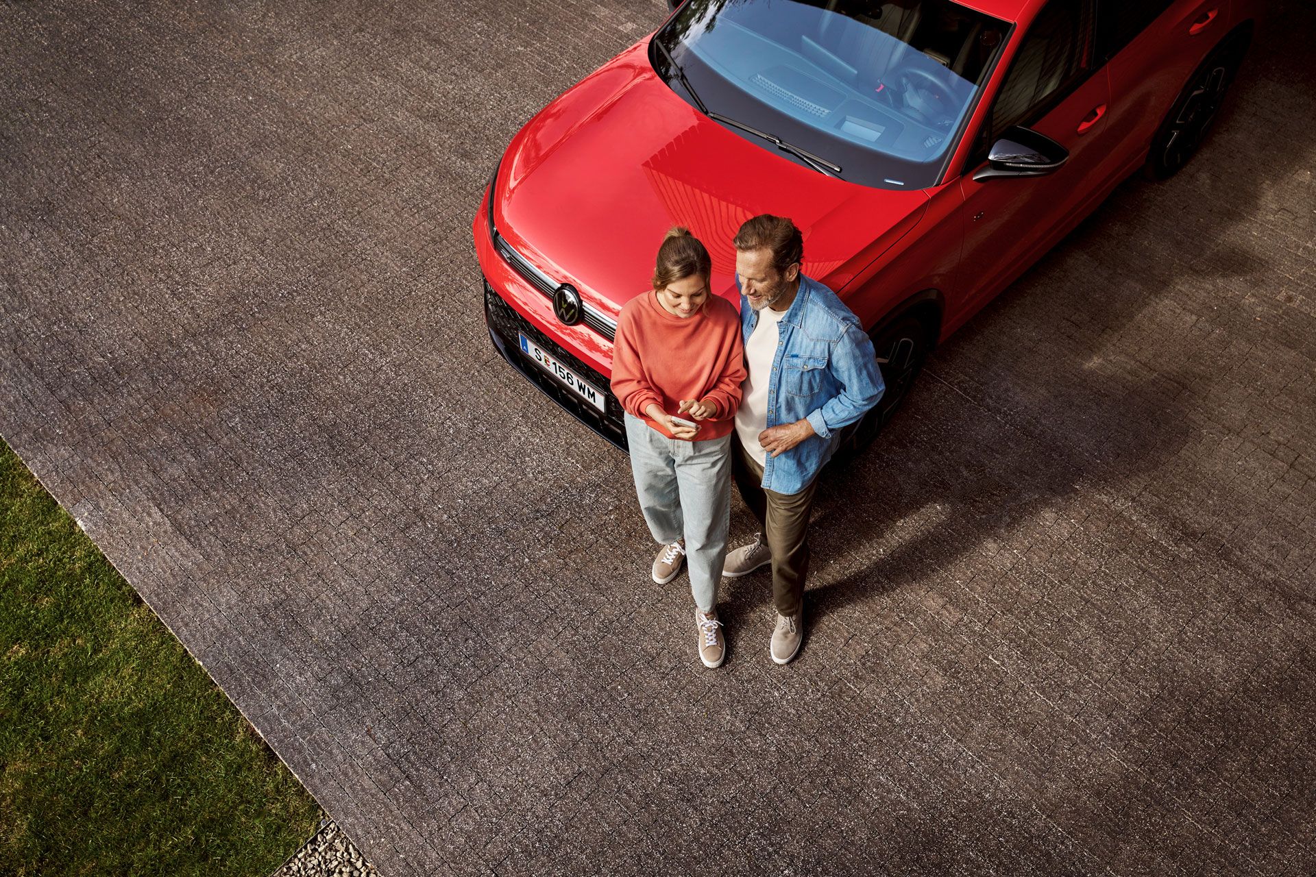Eine Frau und ein Mann stehen vor einem Tiguan und schauen gemeinsam auf ein Handy.