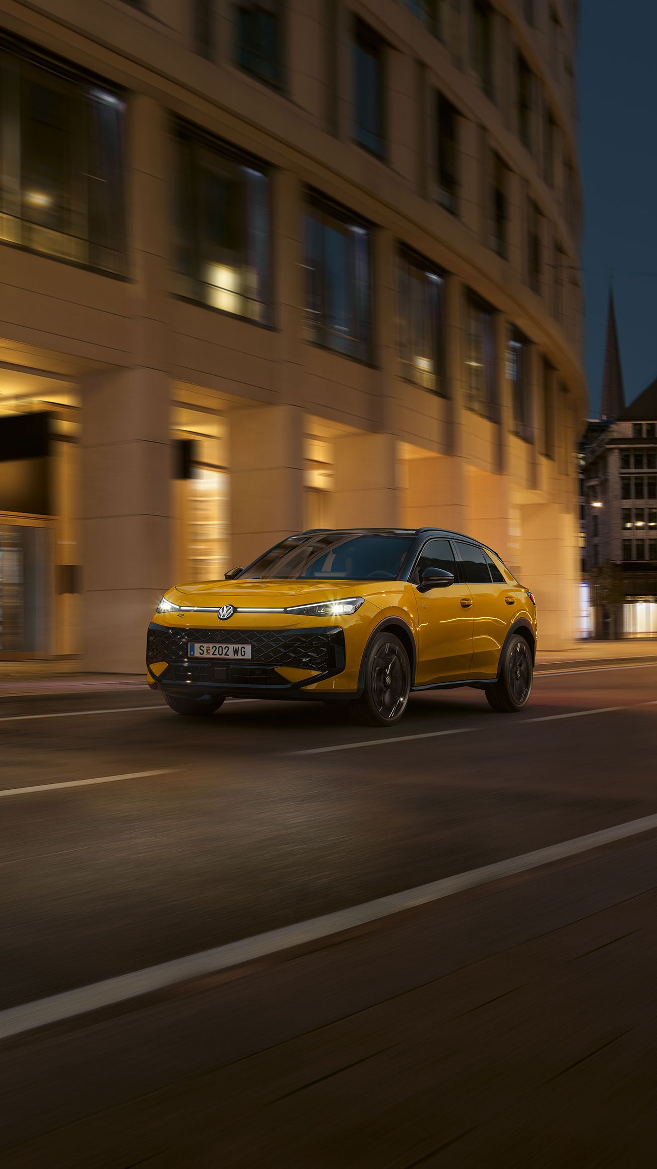 Ein gelber VW T-Roc R-Line fährt nachts durch eine urbane Umgebung.