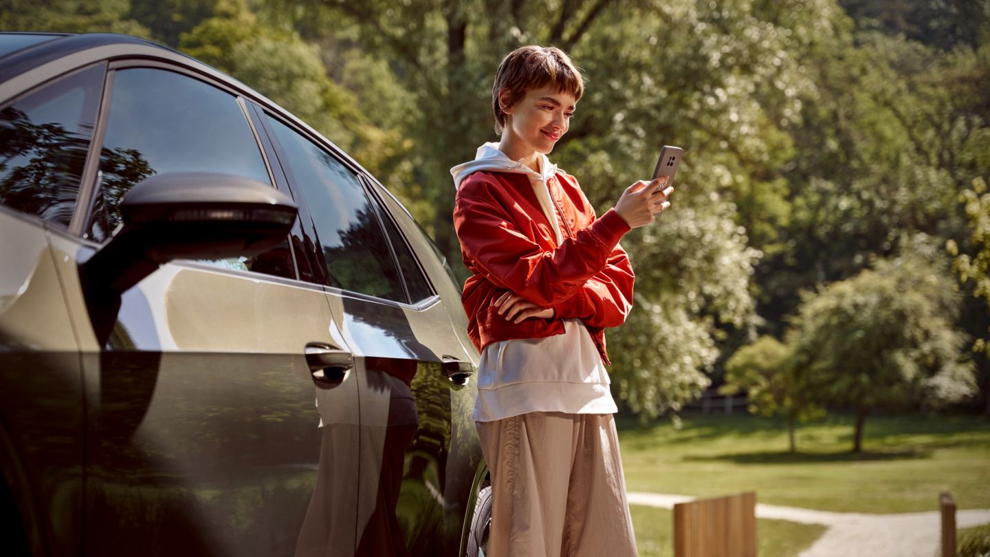 Eine Frau mit einem Smartphone steht neben ihrem ID.3