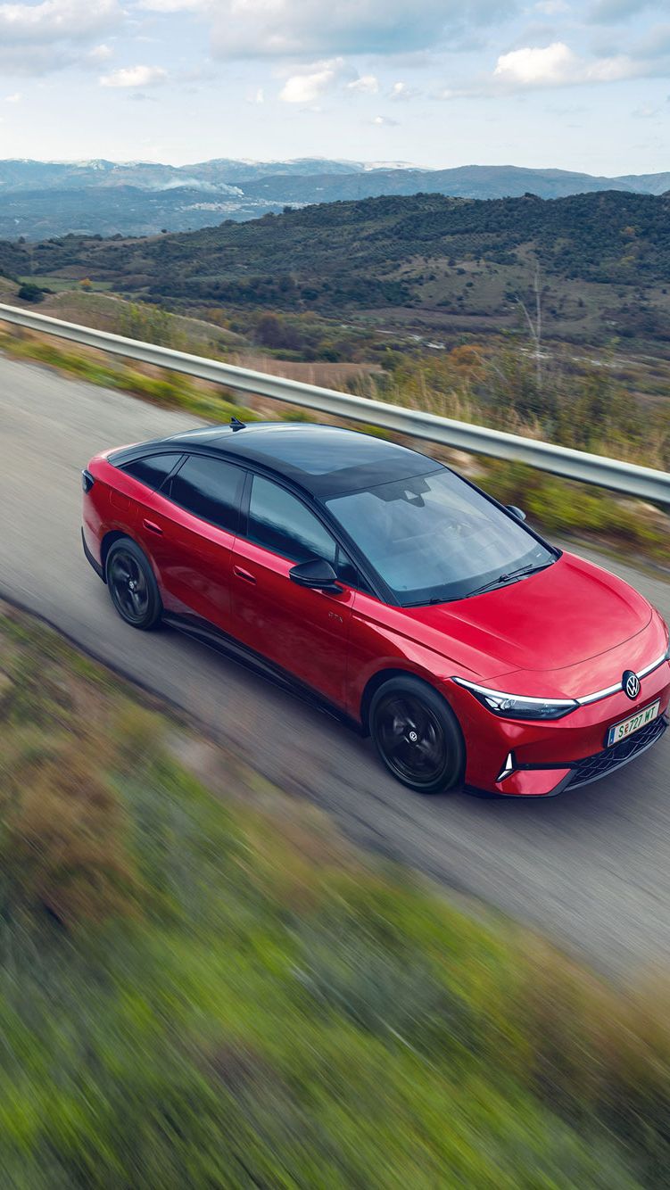 Blick auf die aerodynamisch gestaltete Front eines roten VW ID.7 GTX, der durch eine Berglandschaft fährt.