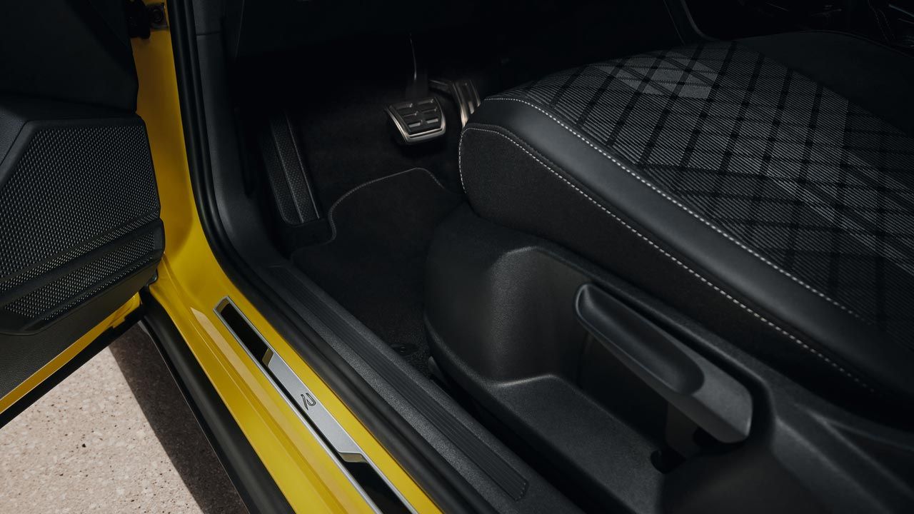 Blick auf unteren Teil des Fahrersitzes des gelben VW T-Cross bei geöffneter Vordertür mit der Einstiegsleiste aus gebürstetem Edelstahl.