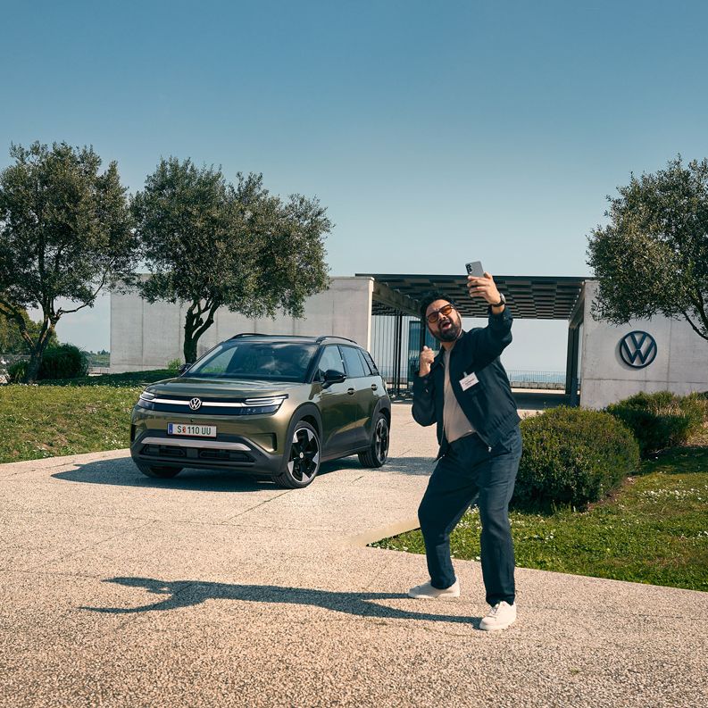 Ein Mann macht jubelnd ein Selfie vor dem grünen VW ID. Cross der vor einem Gebäude parkt.