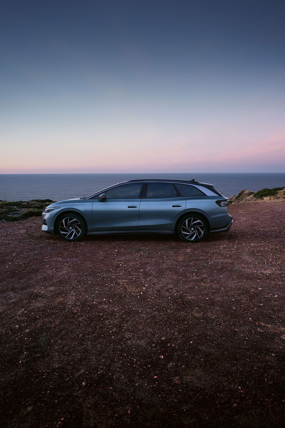 Seitenansicht des VW ID.7 in der Farbe Stonewashed Blue geparkt an der Küste mit Sonnenuntergang