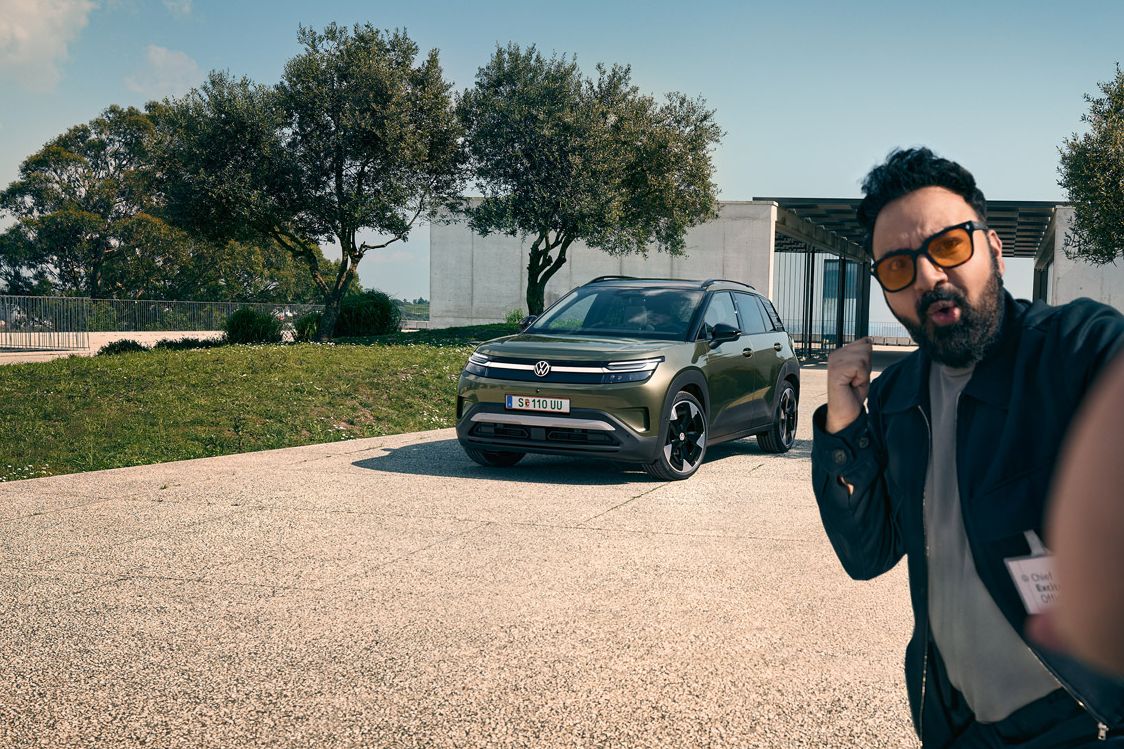 Ein Mann macht ein Selfie mit einem grünen VW ID. Cross, der auf der Auffahrt eines Gebäudes parkt.