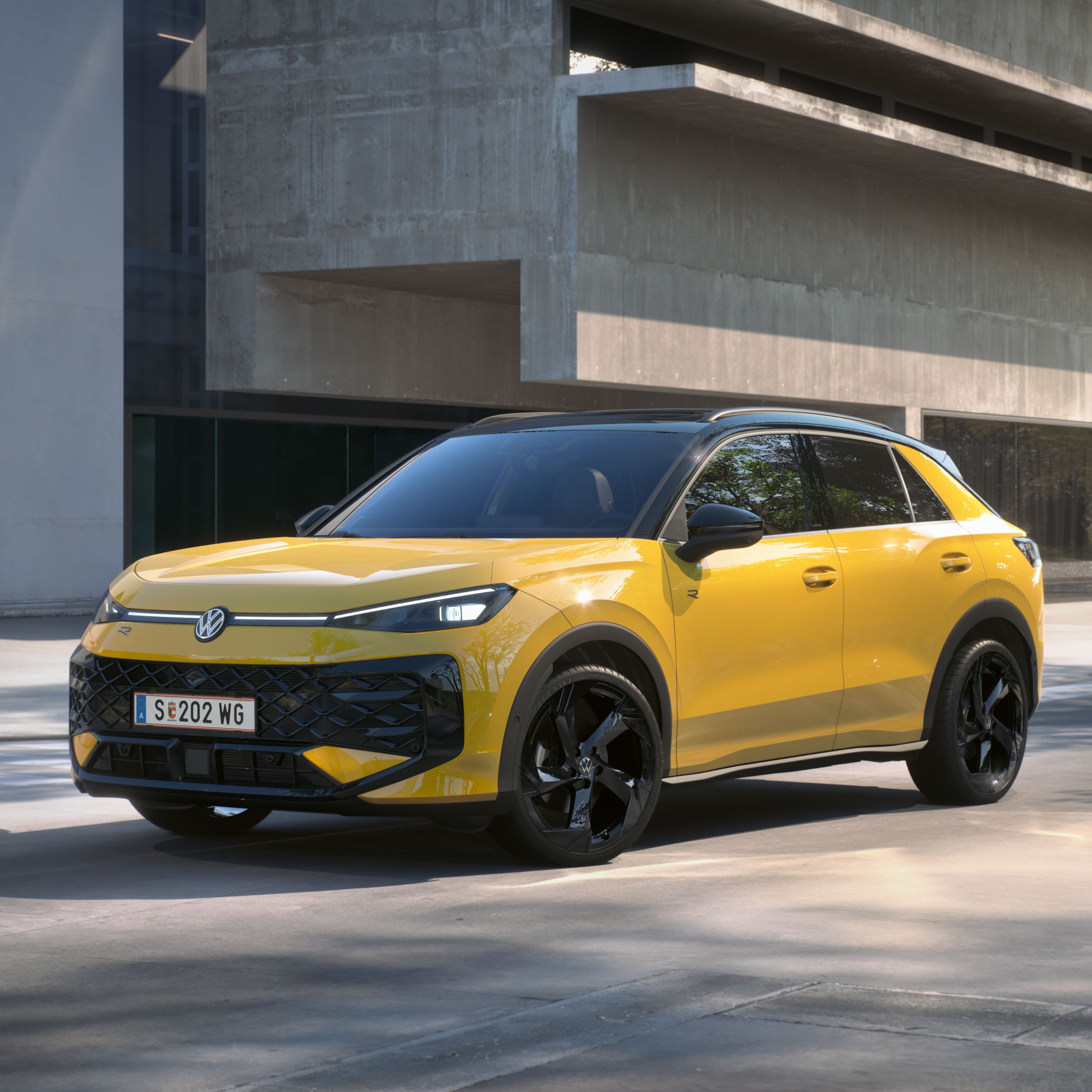 Eine gelber Volkswagen T-Roc R-Line steht in 3/4-Frontansicht vor einem Gebäude.
