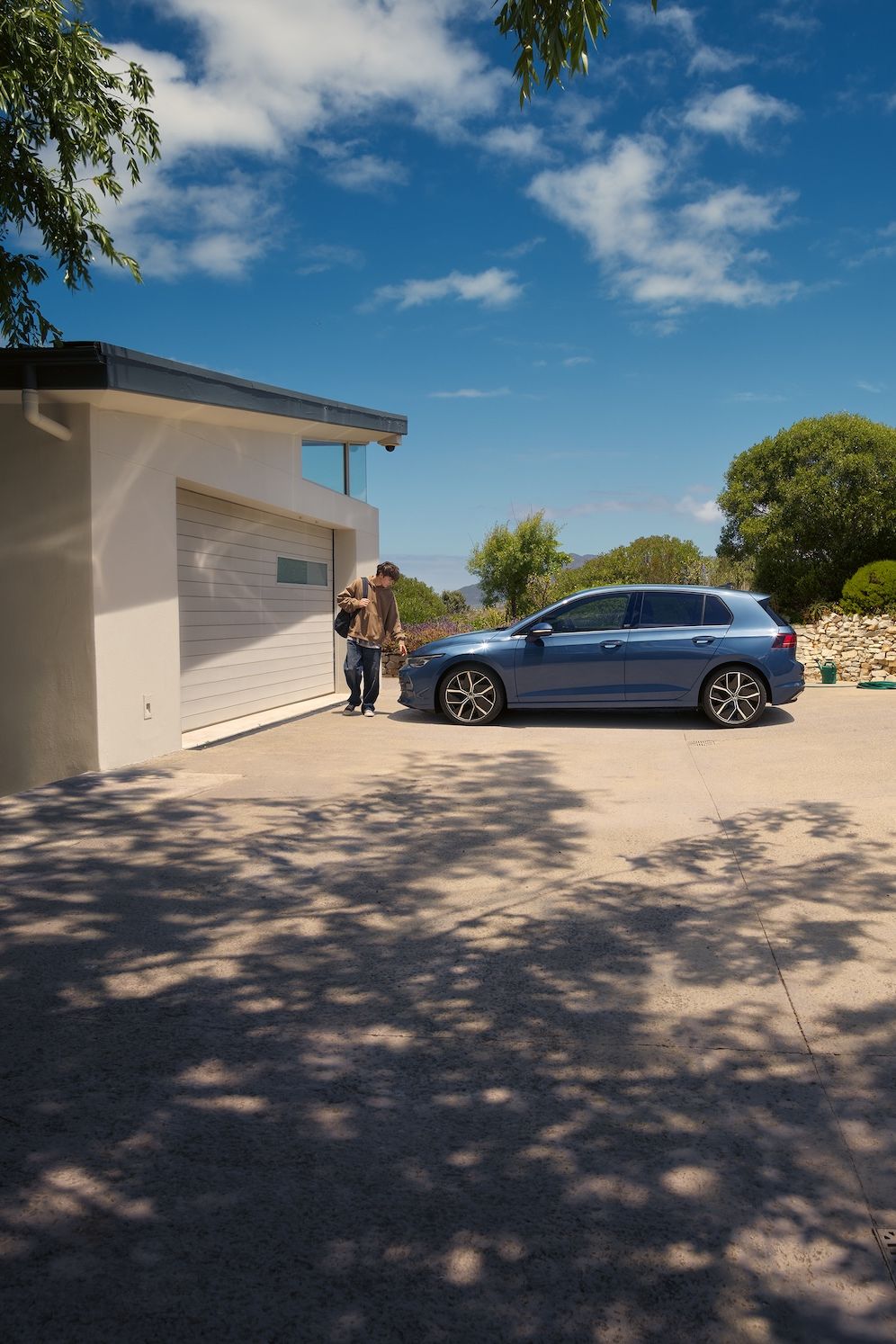 Ein junger Mann geht an einem blauen VW Golf vorbei