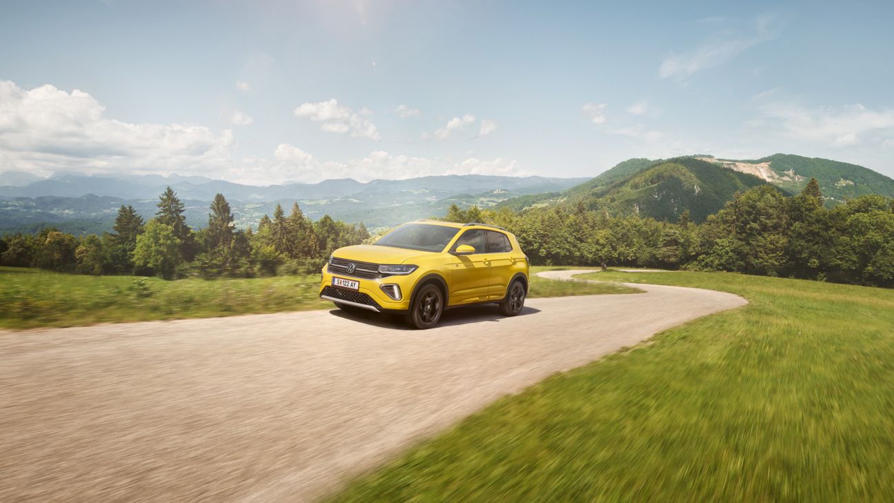 Ein gelber VW T-Cross auf einer Straße in hügeliger Landschaft.
