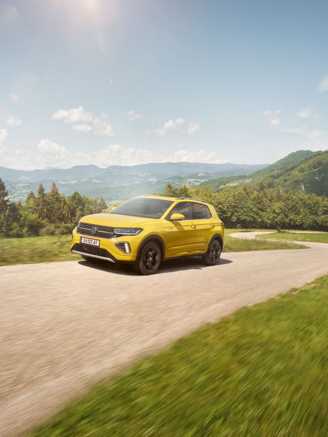 Ein gelber VW T-Cross auf einer Straße in hügeliger Landschaft.