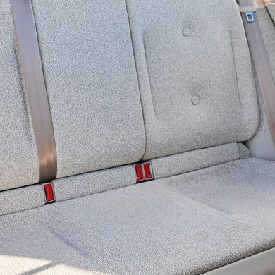 Bild eines Rücksitzes in einem Auto. Die Sitze sind mit einem hellen Stoff bezogen und haben zwei Sicherheitsgurte. Durch das Fenster sieht man eine Strandpromenade.