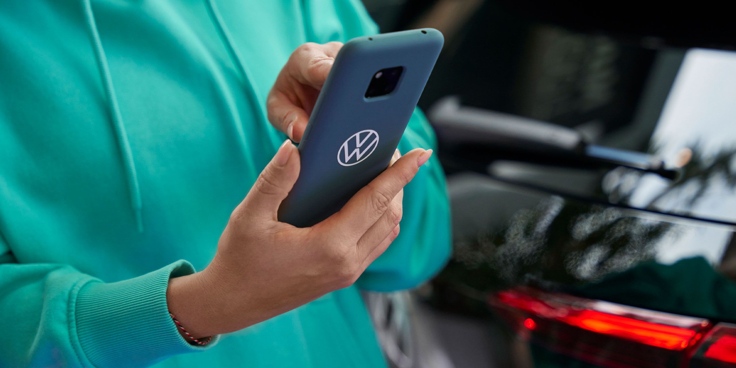 Eine Frau tippt in ihr Smartphone. Auf der blauen Schutzhülle ist das Volkswagen Logo abgebildet.