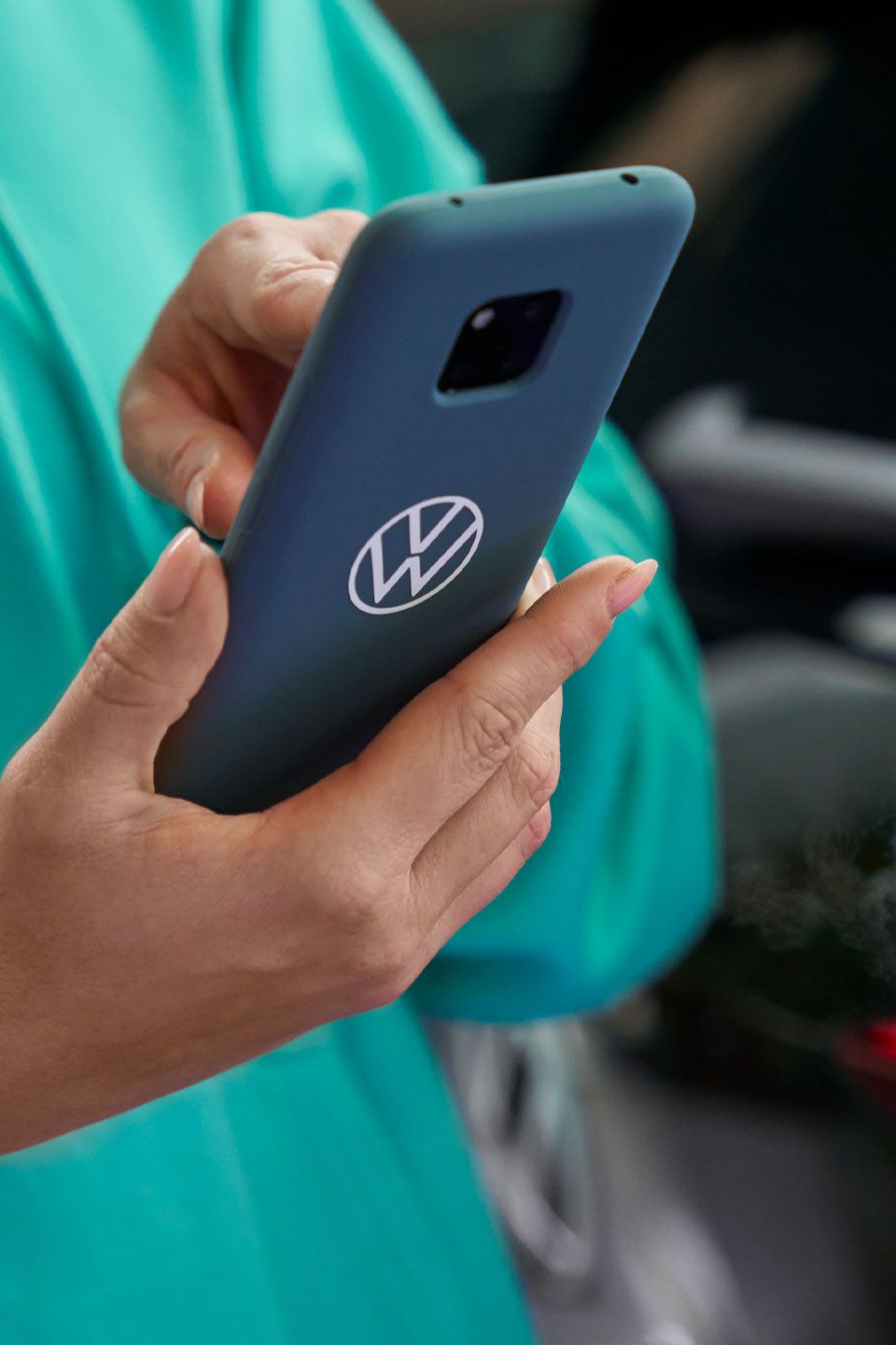 Eine Frau tippt in ihr Smartphone. Auf der blauen Schutzhülle ist das Volkswagen Logo abgebildet.